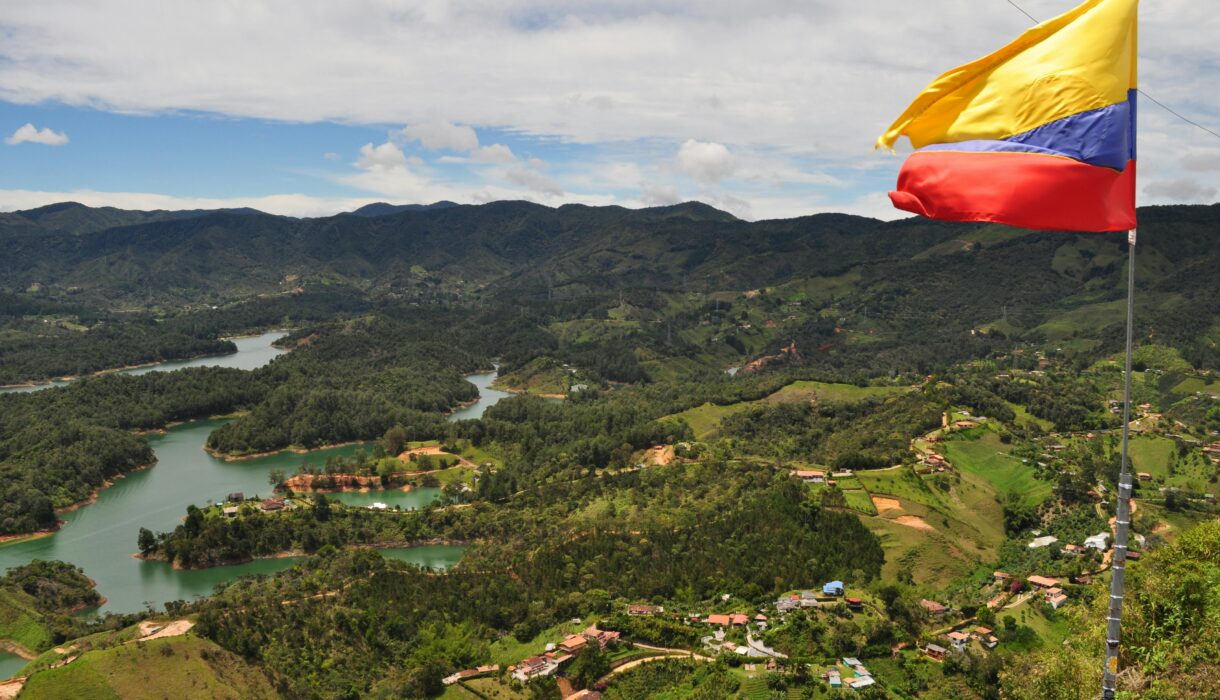 Aerial view of the Colombian flag waving over lush landscapes and winding rivers in the Andes mountains.